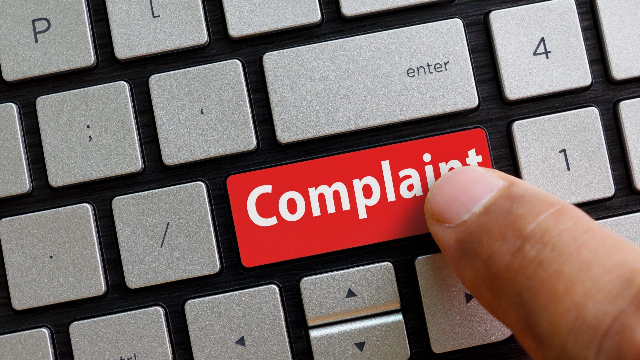 a finger pressing the red 'complaint' button on a keyboard