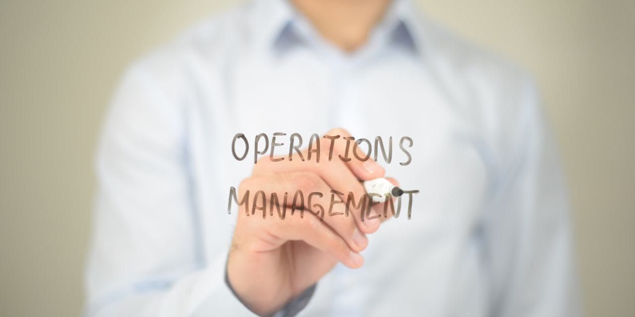 person writing 'operations management' on the glass with a marker
