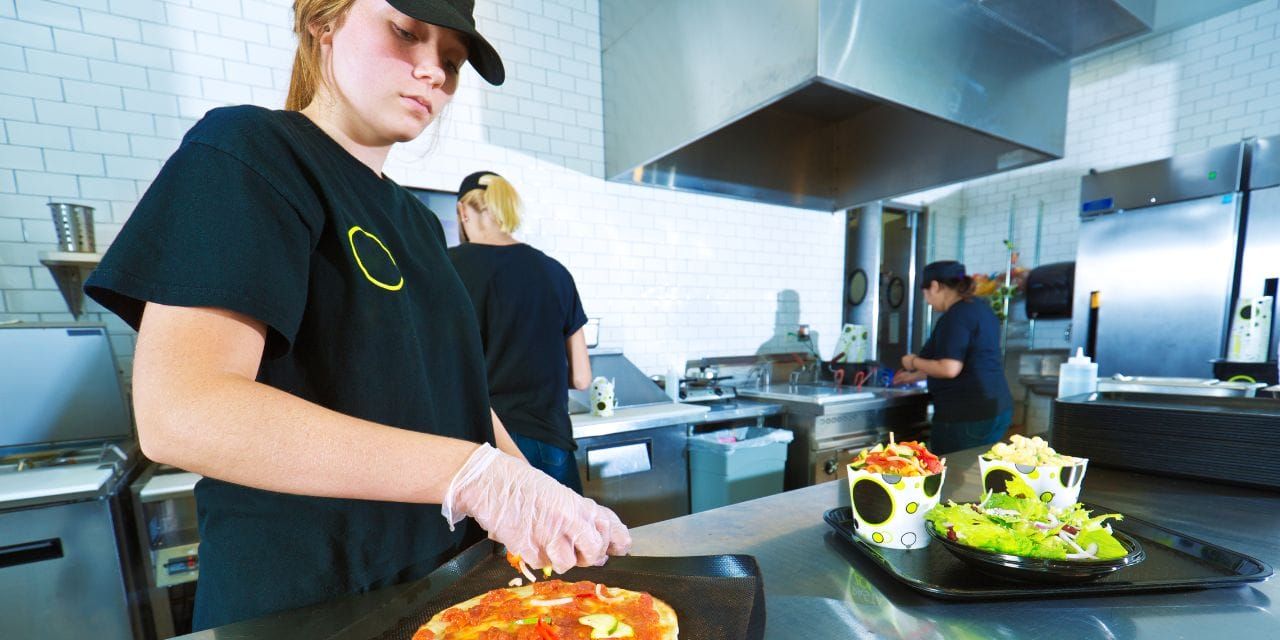 young cook prepping pizza in a restaurant kitchen