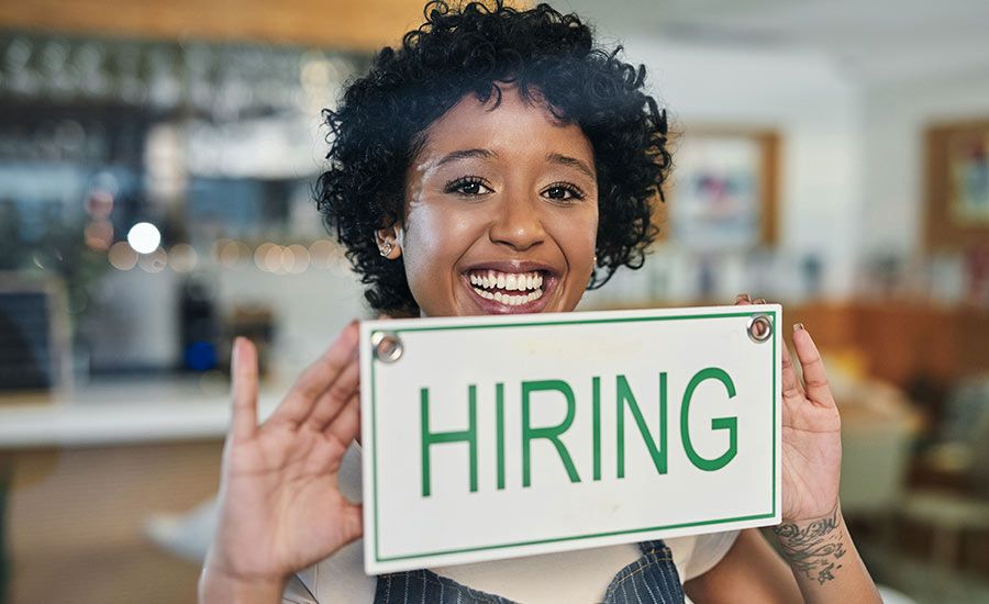 A smiling young African American woman holding up a sign that says "hiring".